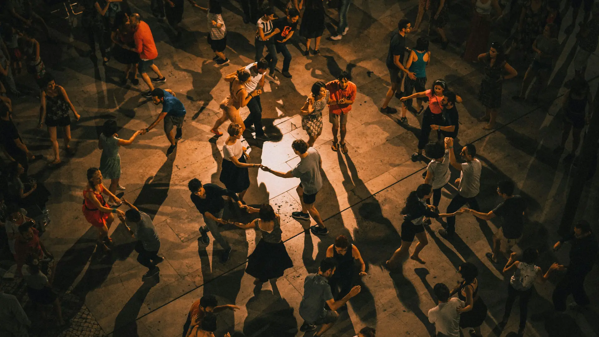 Vista desde arriba de una social al aire libre llena de parejas bailando bajo una luz cálida y tenue